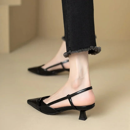 Black kitten heel shoes worn with black jeans on a beige floor.