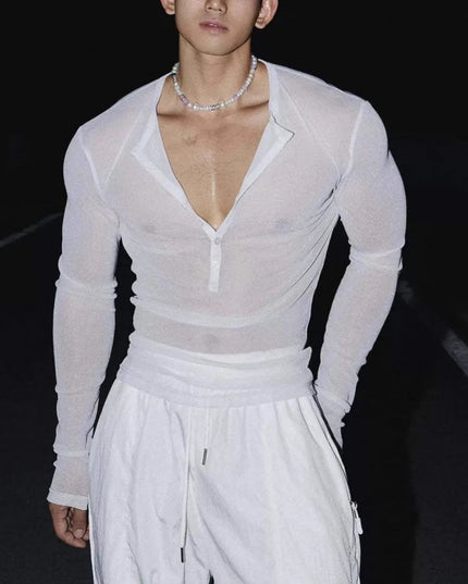 Person wearing a sheer white long-sleeve top and white pants on a dark background