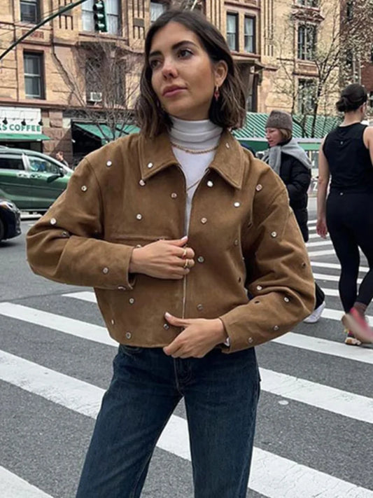 Woman wearing a brown jacket with pearl embellishments on a city street.