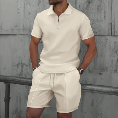 Man wearing a beige polo shirt and shorts set against a textured wall.