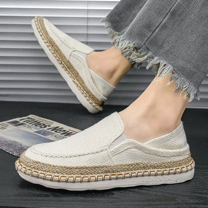 White loafers with jute trim worn by a person on a dark surface.
