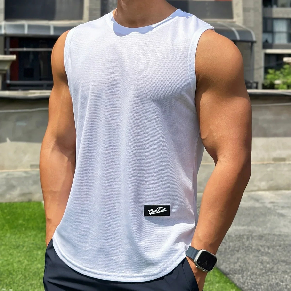 Person wearing a white sleeveless shirt with a brand logo, standing outdoors.