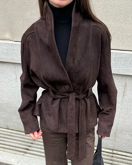 Person wearing a brown suede jacket standing against a gray wall.
