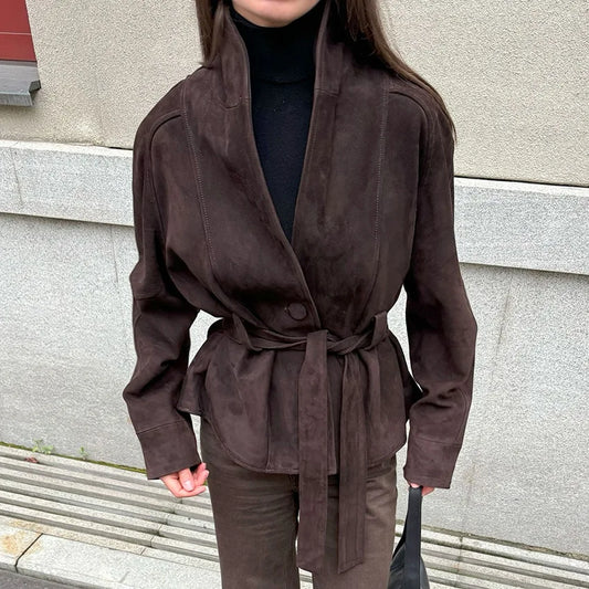 Person wearing a brown suede jacket standing against a gray wall.