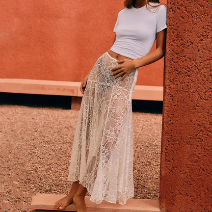 Woman wearing a white lace skirt and crop top against a textured wall.