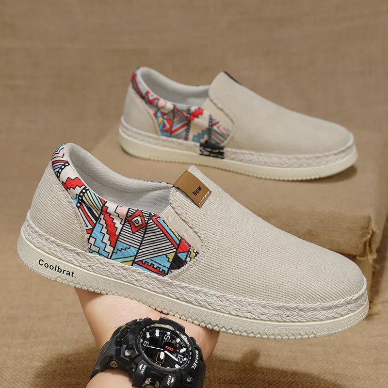 Beige slip-on shoes with colorful patterned straps on a beige surface, wearing a black watch.