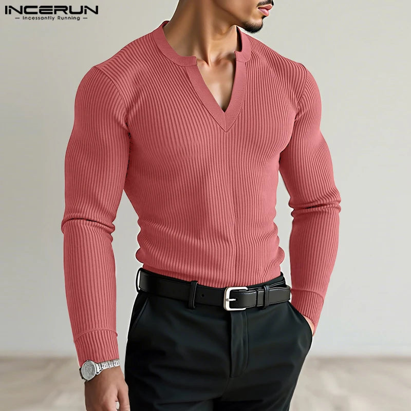 Man wearing a pink ribbed sweater and black pants with a neutral background