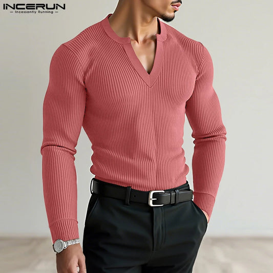 Man wearing a pink ribbed sweater and black pants with a neutral background