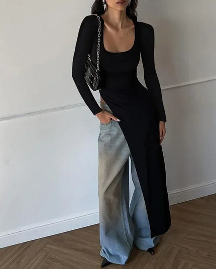 Woman wearing a black top and light blue pants against a white wall.