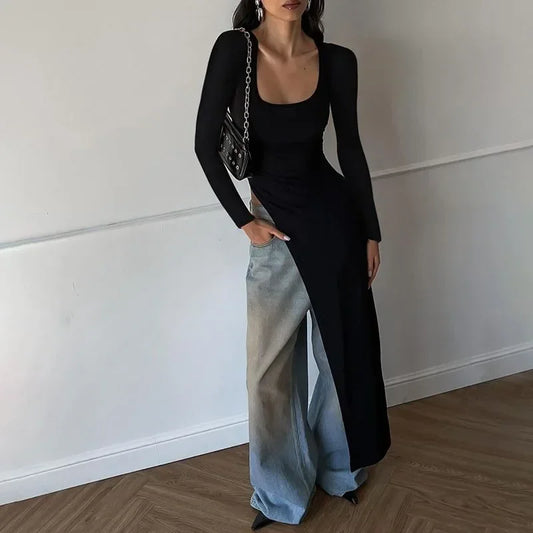 Woman wearing a black top and light blue pants against a white wall.