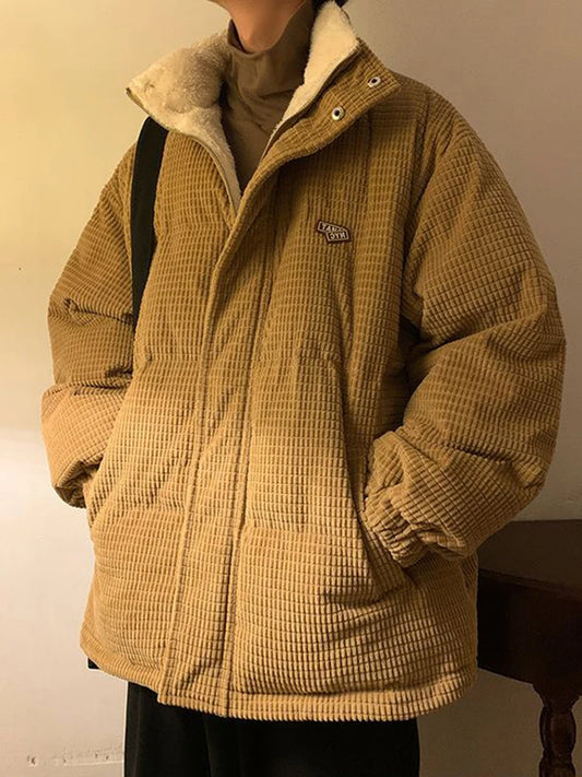 Person wearing a mustard yellow corduroy jacket with a brand logo, standing against a neutral background.