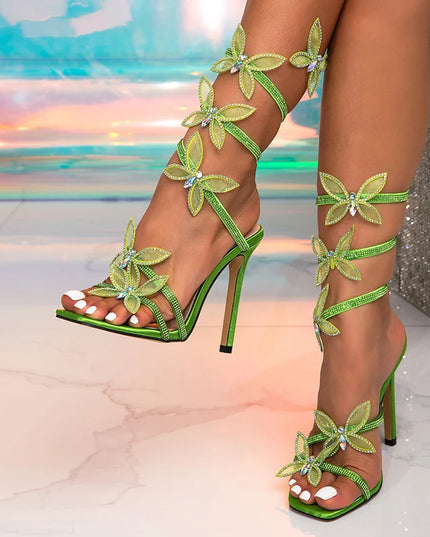 Green high-heeled sandals with floral designs on a blurred background