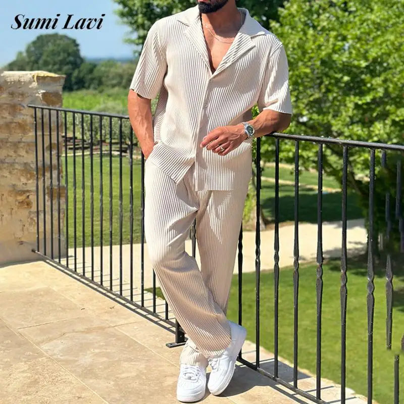 Man in a beige outfit standing on a balcony with greenery in the background