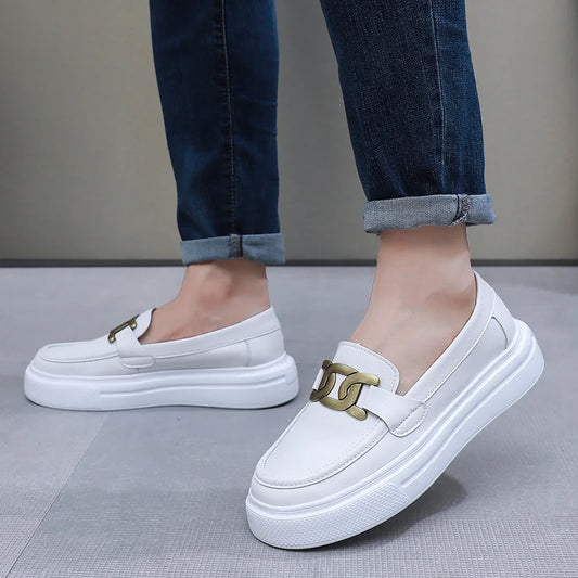White loafers with gold accents worn by a person on a gray floor.