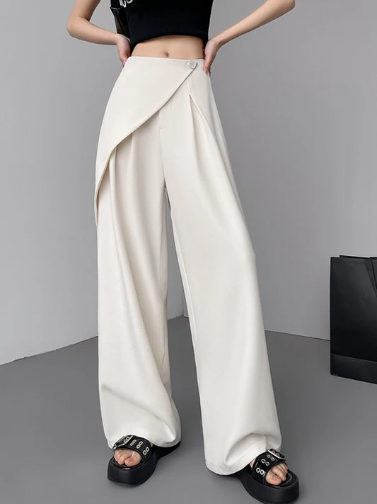 Person wearing white wide-leg pants with a black top and sandals on a gray background