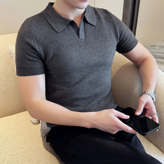 Person wearing a gray polo shirt sitting on a beige couch holding a phone.