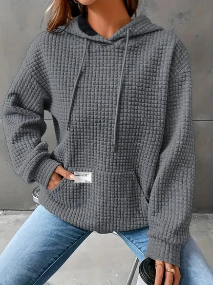 Person wearing a gray textured hoodie with a visible brand label, sitting against a neutral background.