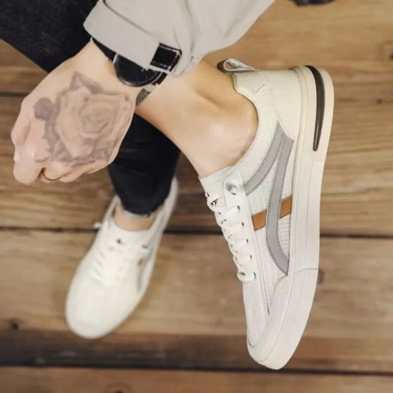 White sneakers with gray accents worn by a person sitting on a wooden floor.