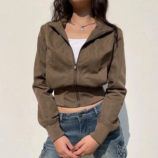 Person wearing a brown jacket and blue jeans against a plain background