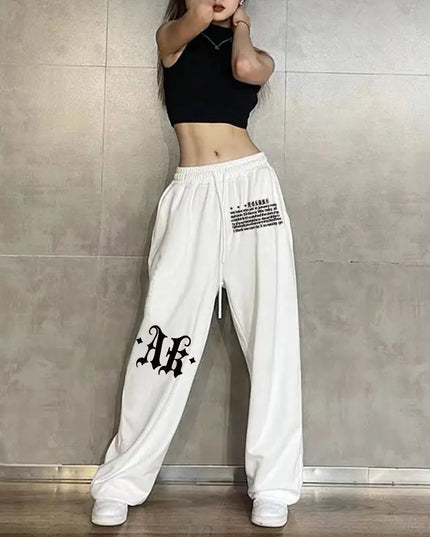 Person wearing white pants with black text and a black top against a gray tiled wall.