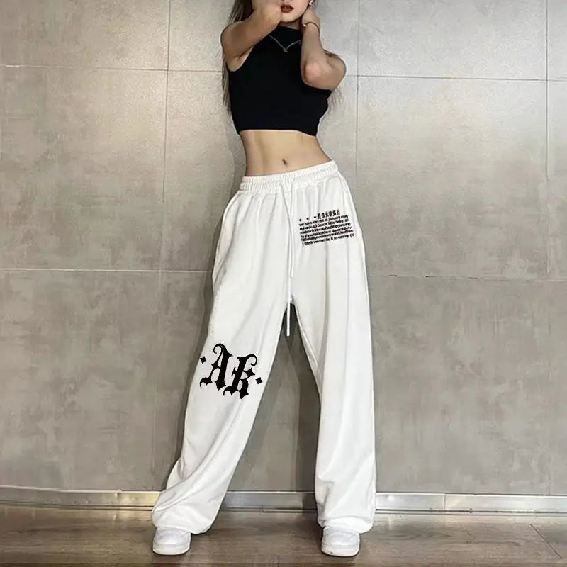 Person wearing white pants with black text and a black top against a gray tiled wall.