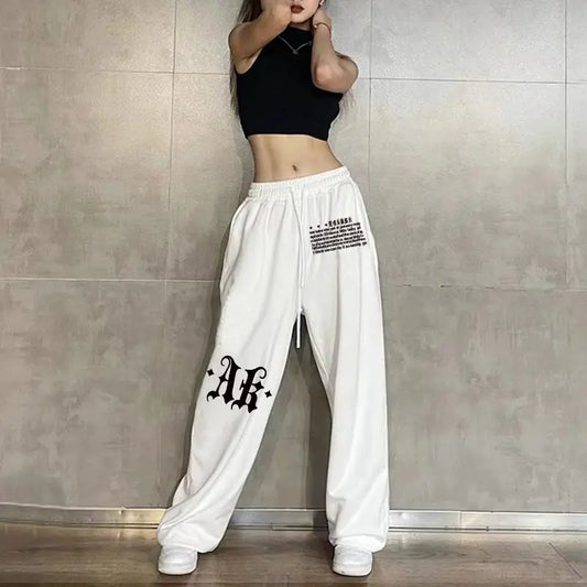 Person wearing white pants with black text and a black top against a gray tiled wall.