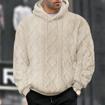 Person wearing a beige cable knit hoodie with a blurred background