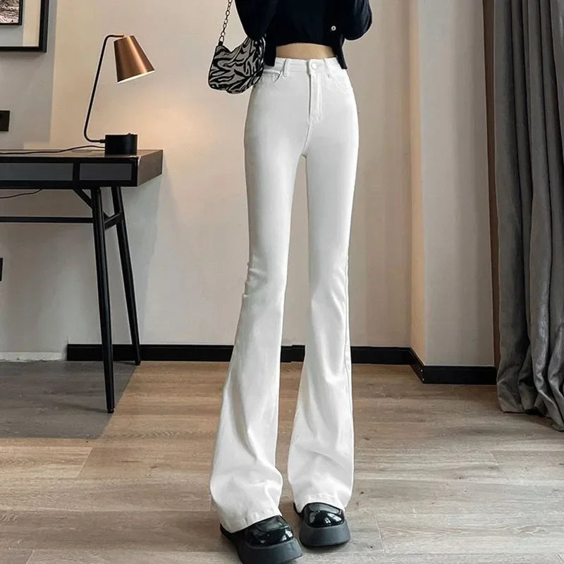 Person wearing white flared jeans in a room with a desk and lamp.