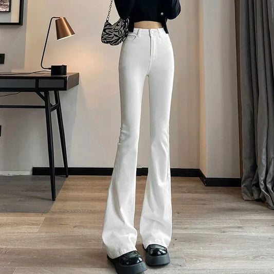 Person wearing white flared jeans in a room with a desk and lamp.