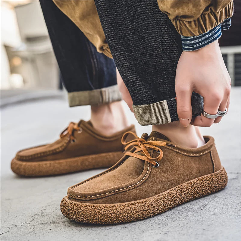 Brown suede shoes worn with dark jeans on a concrete surface