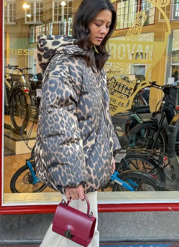 Woman in leopard print coat holding a red handbag in front of a store with bicycles outside.