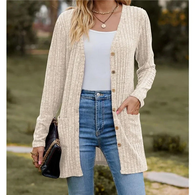 Woman wearing a beige cardigan, white top, and blue jeans outdoors.