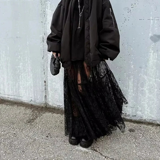 Person wearing a dark outfit with a lace skirt against a textured wall.
