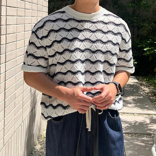 Person wearing a black and white patterned sweater against a light brick wall.
