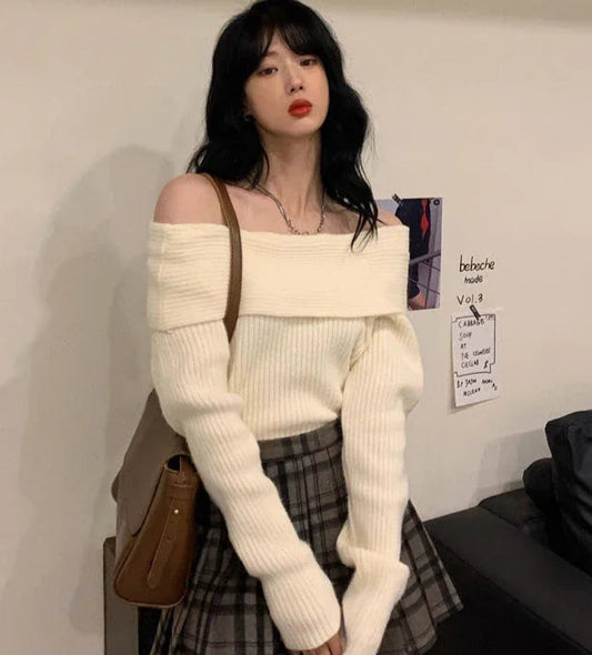 Woman wearing a white off-shoulder sweater and plaid skirt in an indoor setting.