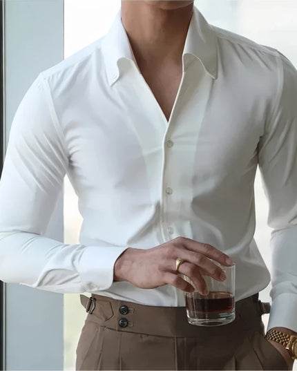 Person wearing a white dress shirt and brown pants holding a glass with a dark liquid.