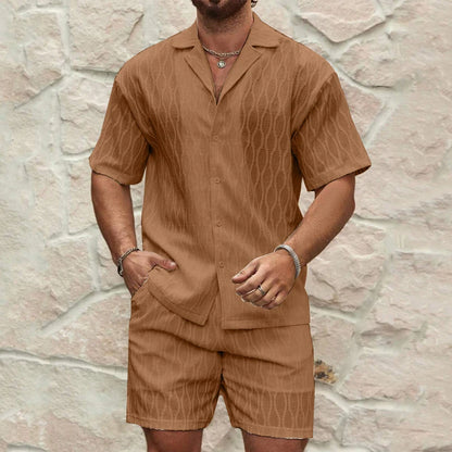 Man wearing a brown patterned shirt and shorts set against a stone wall.