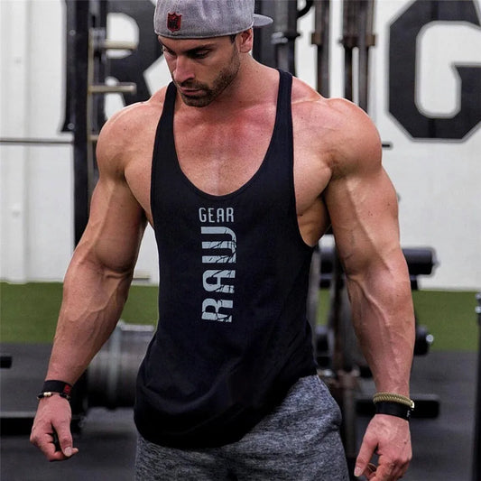 Muscular man in a gym wearing a black tank top with visible branding.