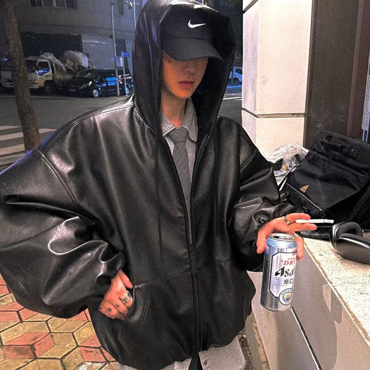 Person in a black leather jacket and hoodie holding a can on a street.