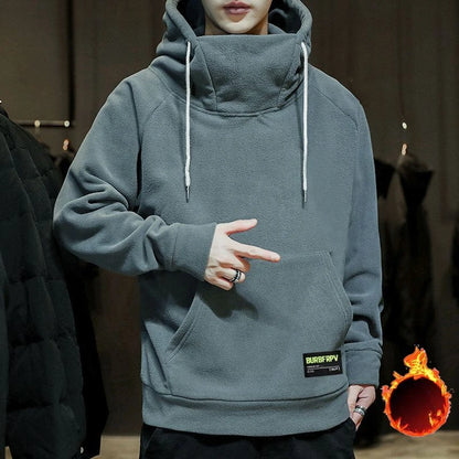 Person wearing a gray hoodie with a brand logo, pointing to the pocket.