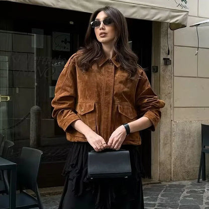 Woman in a brown jacket and sunglasses holding a black clutch in an urban setting.