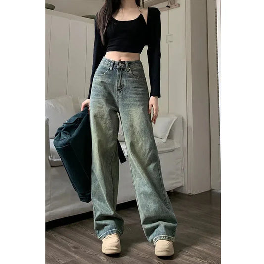 Person wearing high-waisted blue jeans and a black top in a room.