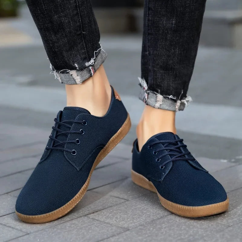 Navy blue casual shoes with brown soles worn with rolled-up jeans on a pavement.