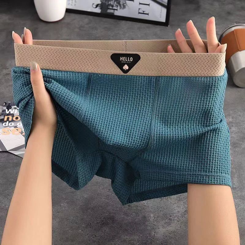 Teal shorts with beige waistband held by hands on a gray surface