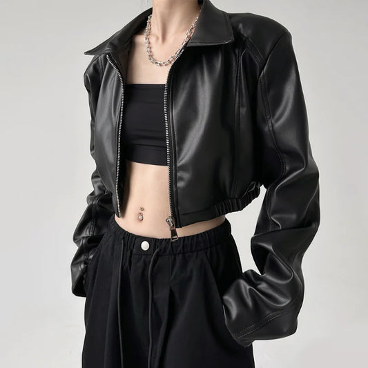 Person wearing a black leather jacket over a black crop top and pants on a gray background