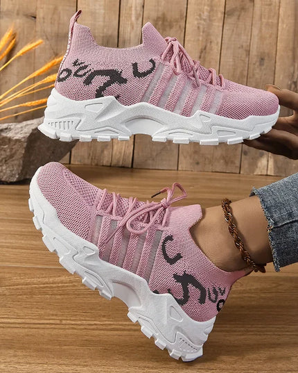 Pink sneakers with white soles worn by a person on a wooden floor.