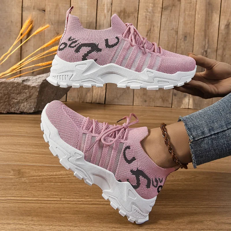 Pink sneakers with white soles worn by a person on a wooden floor.