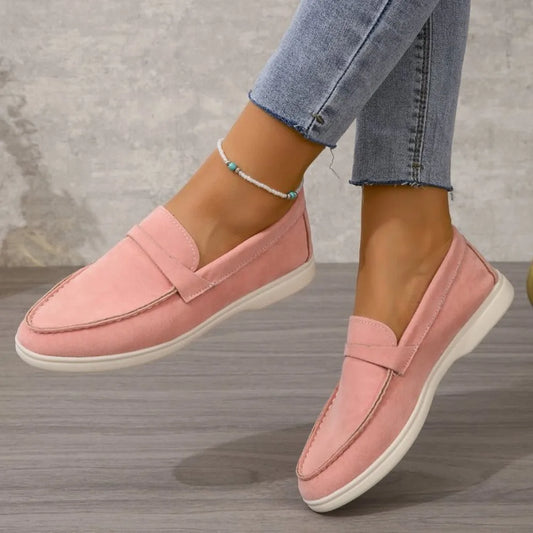 Pink loafers worn with blue jeans on a wooden floor.