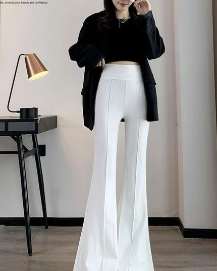Person wearing a black top and white pants in a room with a lamp and desk.